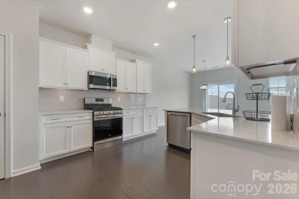 a large kitchen with stainless steel appliances granite countertop a stove a sink a refrigerator and white cabinets with wooden floor