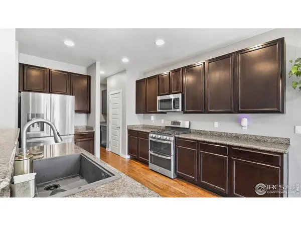 a kitchen with stainless steel appliances kitchen island granite countertop a stove top oven a sink dishwasher and wooden cabinets with wooden floor