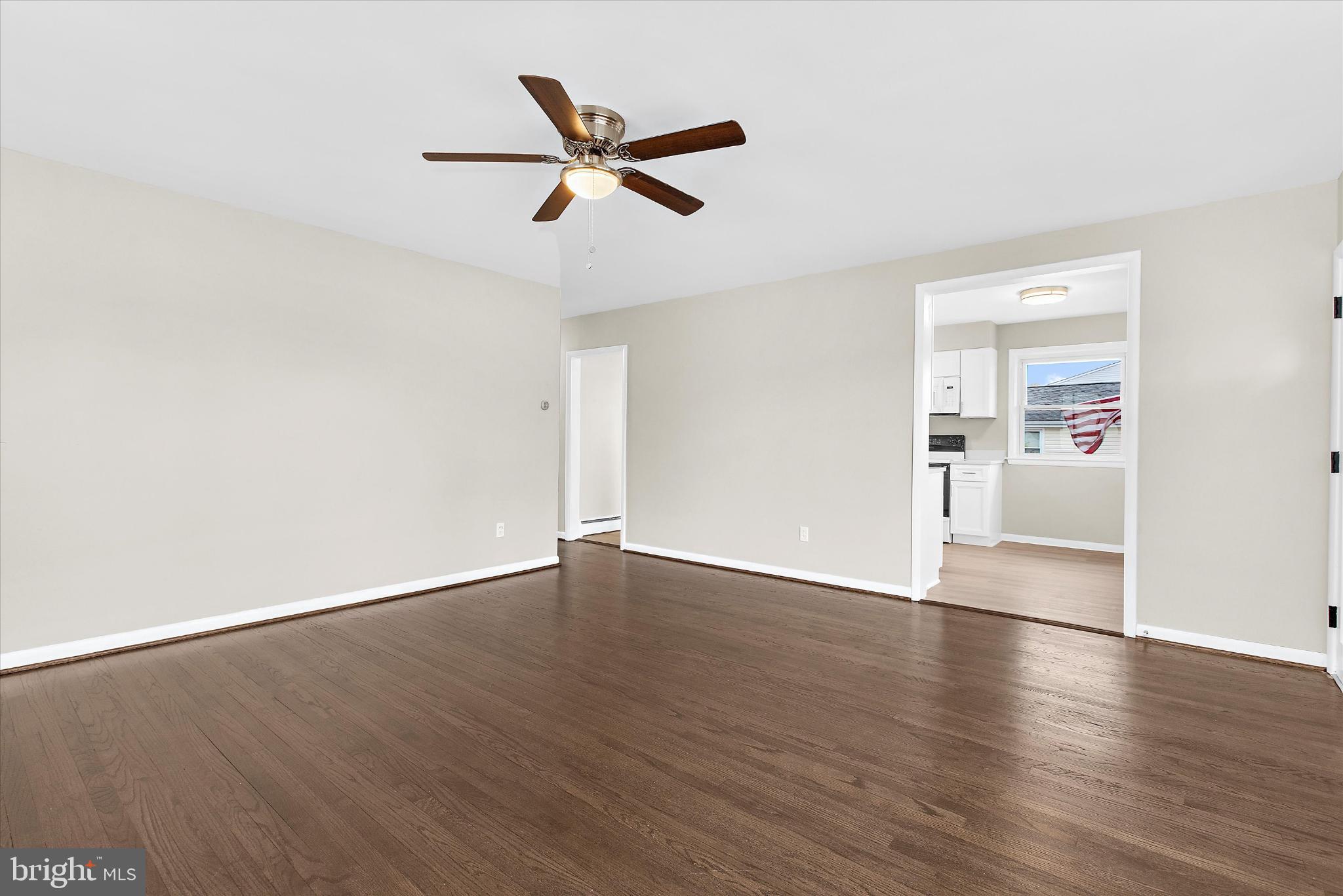 8421 Spring Road Pasadena, MD 21122 - Photo 3 of 30 an empty room with wooden floor a ceiling fan and windows
