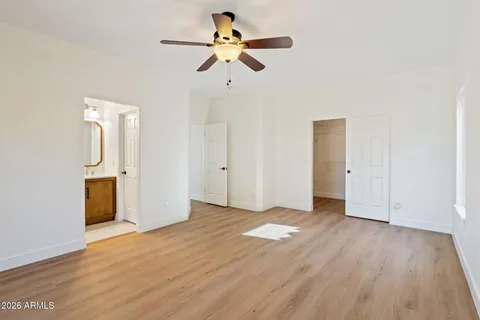 a view of an empty room with wooden floor and a ceiling fan