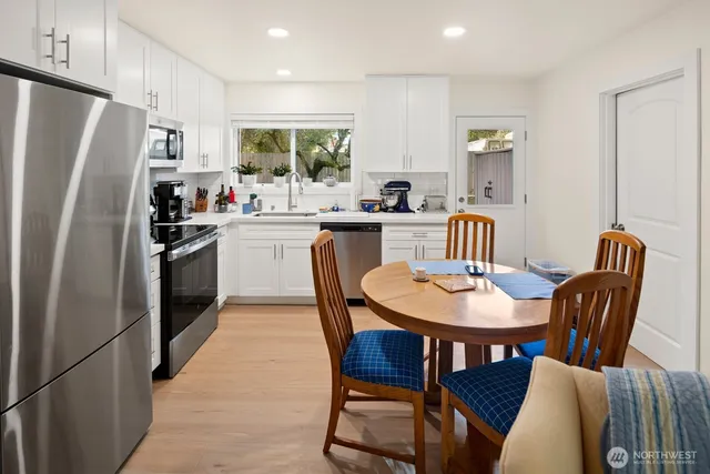 a kitchen with stainless steel appliances granite countertop a sink a stove a refrigerator cabinets and a dining table with wooden floor