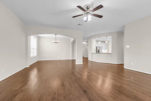 a view of an empty room with wooden floor and a ceiling fan