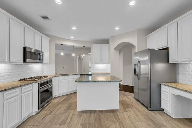 a kitchen with stainless steel appliances granite countertop a stove top oven a refrigerator a sink and dishwasher with wooden floor