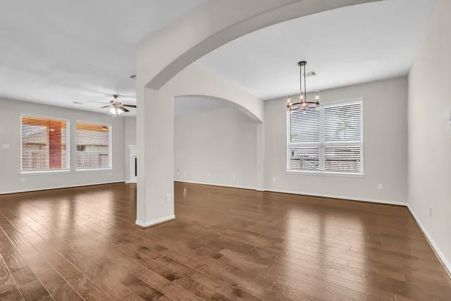 an empty room with wooden floor chandelier and windows