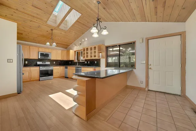 a kitchen with stainless steel appliances a refrigerator a sink dishwasher a stove top oven a dining table and chairs with wooden floor