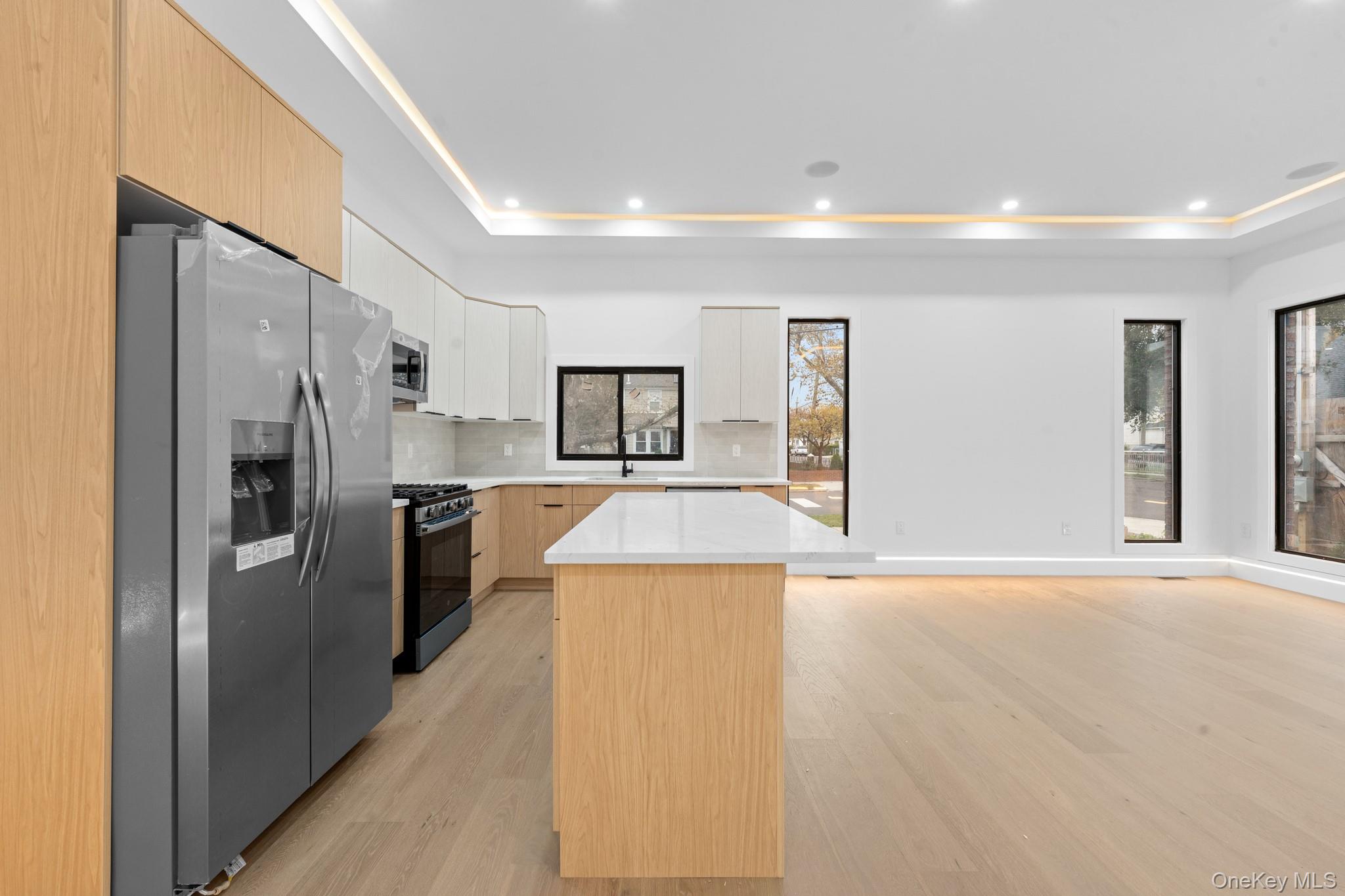 116-20 194th Street Queens, NY 11412 - Photo 5 of 27 Kitchen featuring light brown cabinetry, appliances with stainless steel finishes, a raised ceiling, light wood finished floors, and tasteful backsplash
