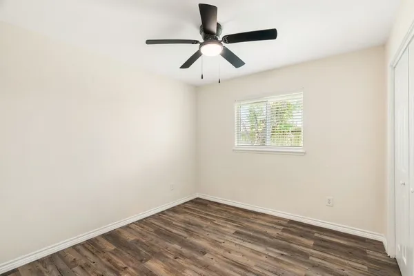 an empty room with wooden floor chandelier fan and windows