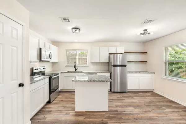 a kitchen with stainless steel appliances granite countertop a refrigerator a stove top oven a sink and dishwasher with wooden floor
