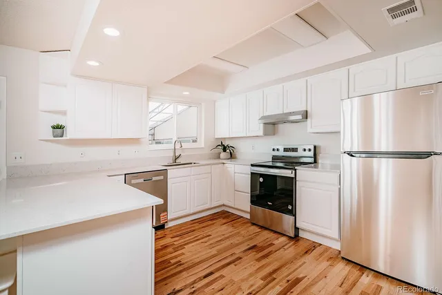 a kitchen with a refrigerator stove and white cabinets with wooden floor