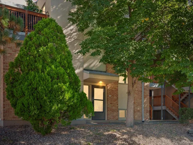 a view of a brick house with plants and large trees