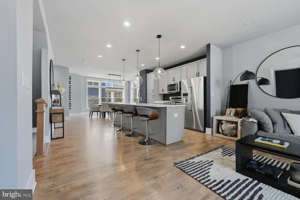 a kitchen with stainless steel appliances kitchen island granite countertop a refrigerator oven a sink a dining table and chairs with wooden floor