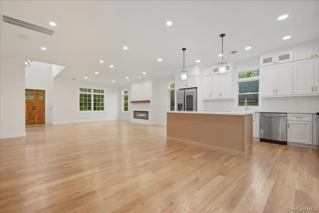 a large white kitchen with kitchen island a sink a stove a refrigerator and white cabinets with wooden floor