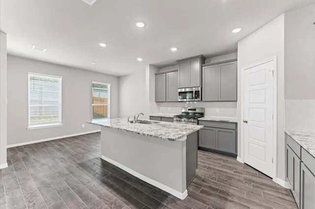 a kitchen with stainless steel appliances granite countertop a stove a sink a refrigerator and white cabinets with wooden floor