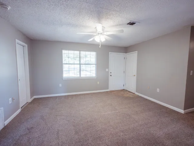 an empty room with chandelier fan and windows
