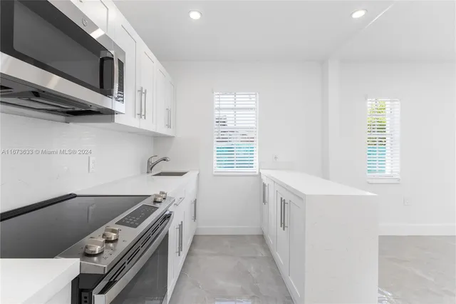 a large white kitchen with stainless steel appliances refrigerator a stove top oven and white cabinets