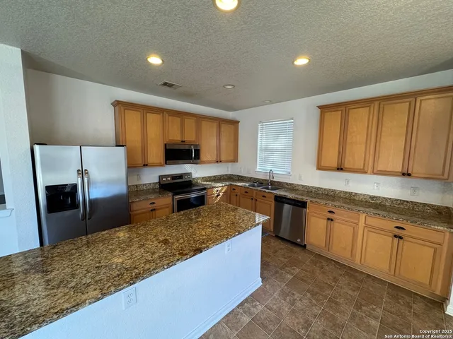 a large kitchen with granite countertop a large counter top a sink a stove and a refrigerator