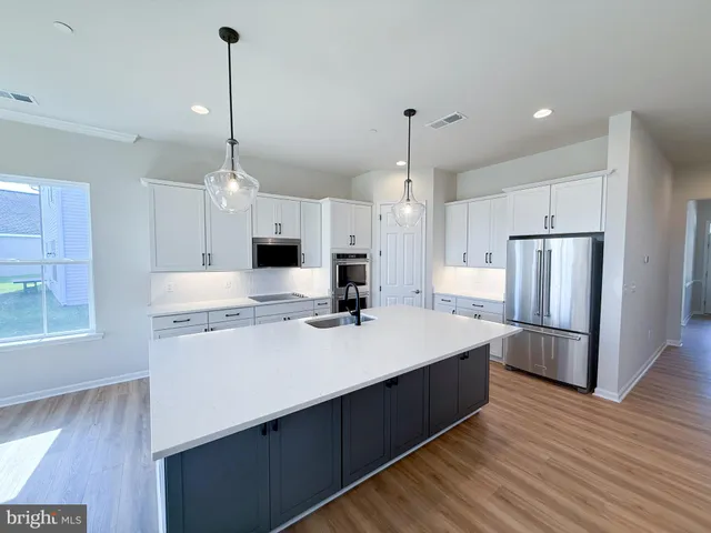 a kitchen with stainless steel appliances kitchen island a refrigerator a sink dishwasher a oven and a dining table with wooden floor