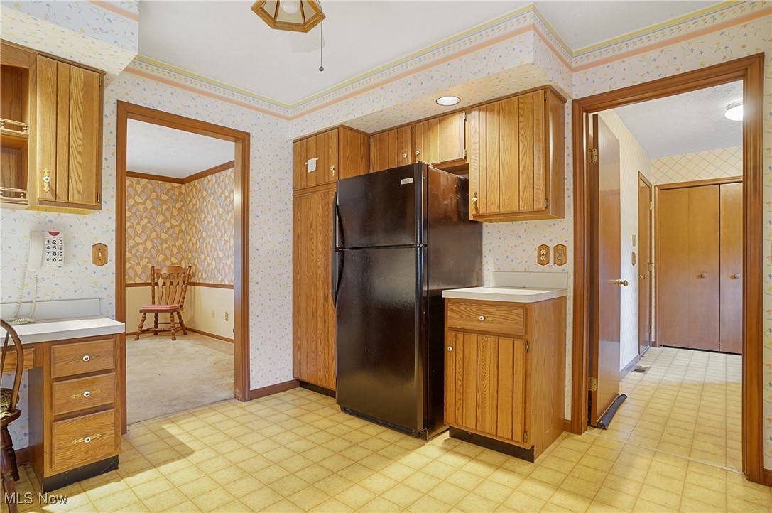 7300 Morley Road Painesville, OH 44077 - Photo 14 of 50 Kitchen featuring light floors, wallpapered walls, freestanding refrigerator, light countertops, and brown cabinets