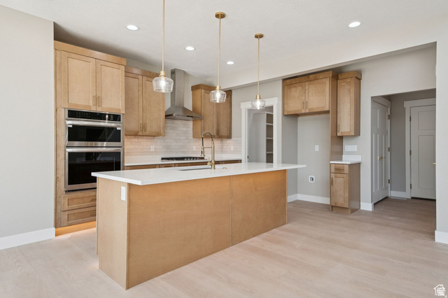 1471 Colbey Loop Santa Clara, UT 84765 - Photo 5 of 45 Spacious kitchen featuring light wood-finish cabinetry, a large center island with a white countertop, stainless steel double wall ovens, a coordinating range hood, and light wood-finish flooring