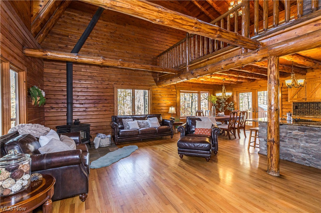 Living room featuring a wood stove, high vaulted ceiling, wood walls, light hardwood / wood-style flooring, and an inviting chandelier