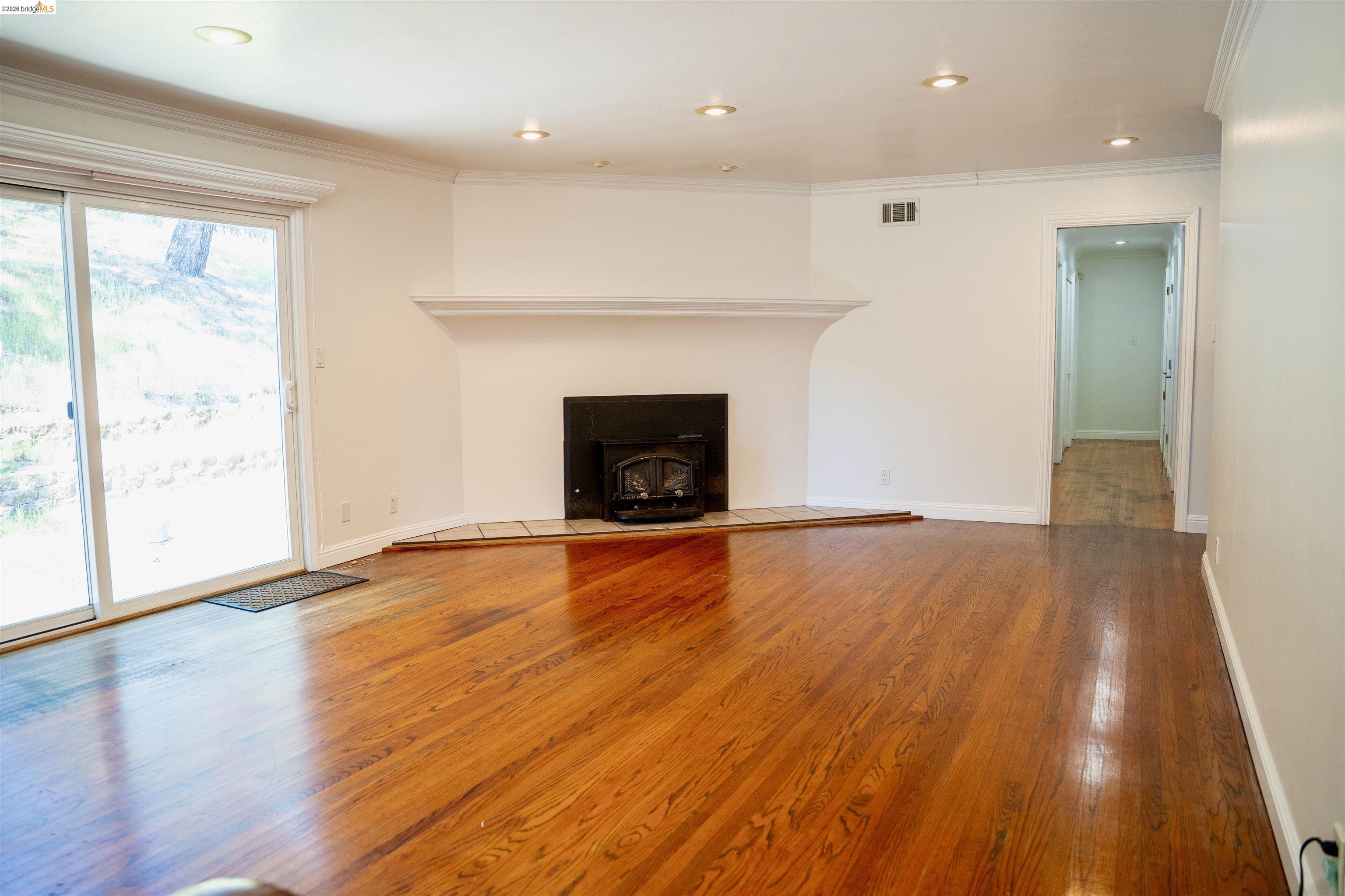 64 Washington Street Novato, CA 94947 - Photo 11 of 21 Spacious living area featuring rich wood-finish flooring, a prominent fireplace with a white mantel, recessed lighting, white baseboards, and a large glass sliding door opening to exterior surroundings