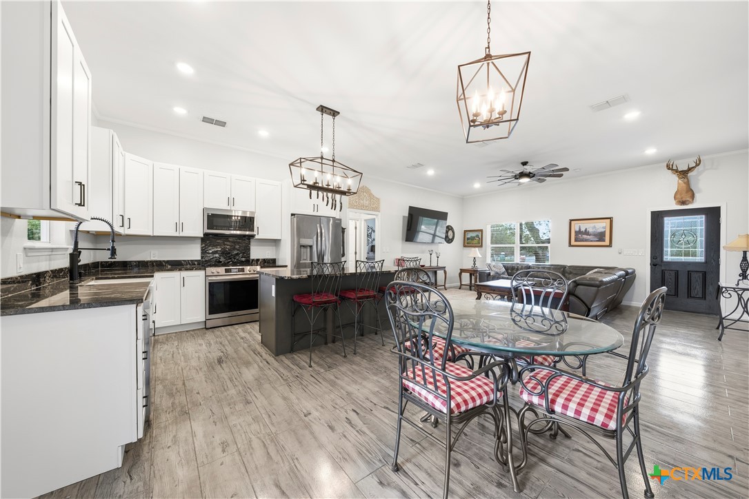 351 Line Camp Loop Spring Branch, TX 78070 - Photo 6 of 27 an open kitchen with stainless steel appliances kitchen island granite countertop a stove a sink a dining table and chairs with wooden floor