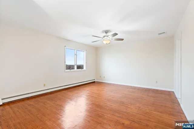an empty room with wooden floor chandelier fan and windows