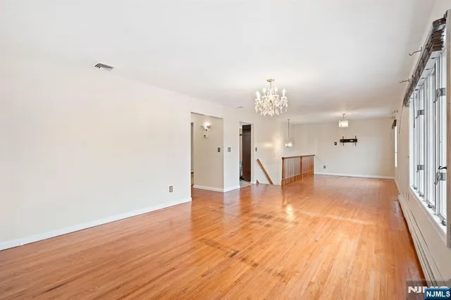 a view of an empty room with wooden floor and a kitchen
