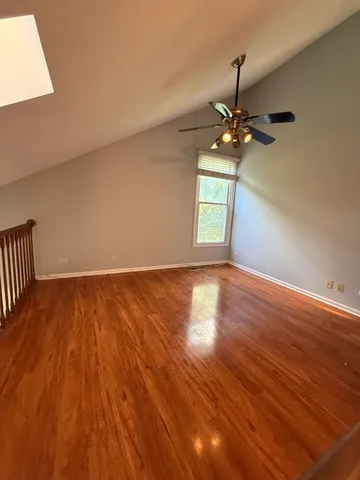 an empty room with wooden floor chandelier fan and windows