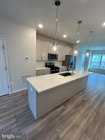 a room with stainless steel appliances kitchen island granite countertop a sink a stove and a wooden floors