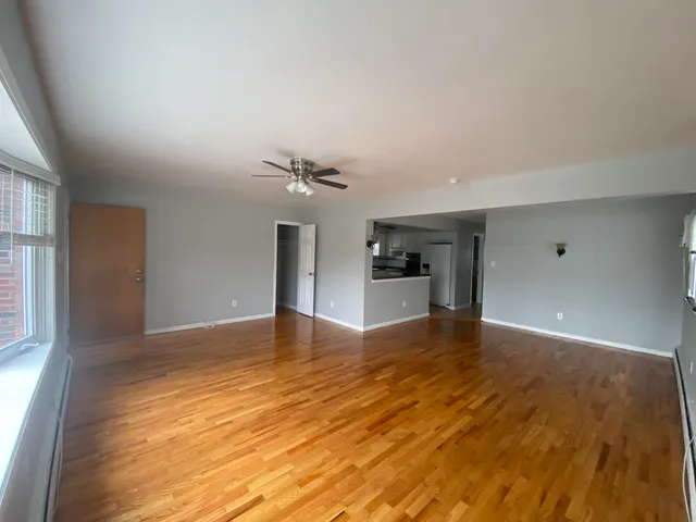 a view of empty room with wooden floor and kitchen view