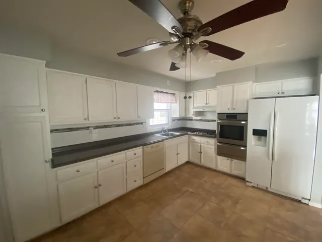 a kitchen with granite countertop a refrigerator a sink and white cabinets