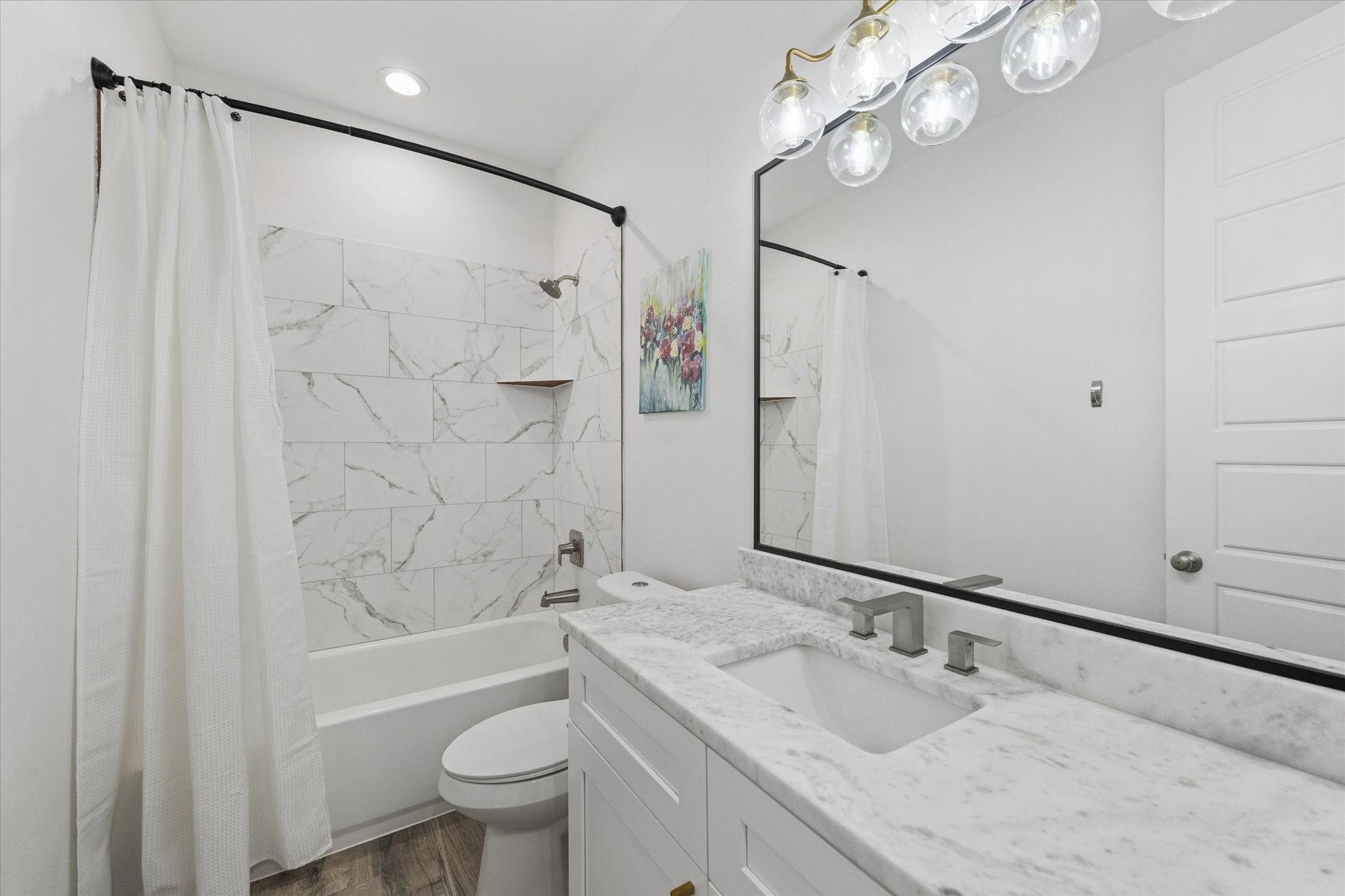 203 Hampton Glen Road Montgomery, TX 77356 - Photo 24 of 35 Every detail in this home reflects high-end quality, as seen in this secondary bathroom. The marble countertops, clear tile in the bathtub area, and custom mirror with dark edging create a harmonious and sophisticated look. Recently installed dark faucets and the brass LED light fixture enhance the space, making it both functional and stylish. This serene bathroom offers a calm and inviting retreat for family members or guests.