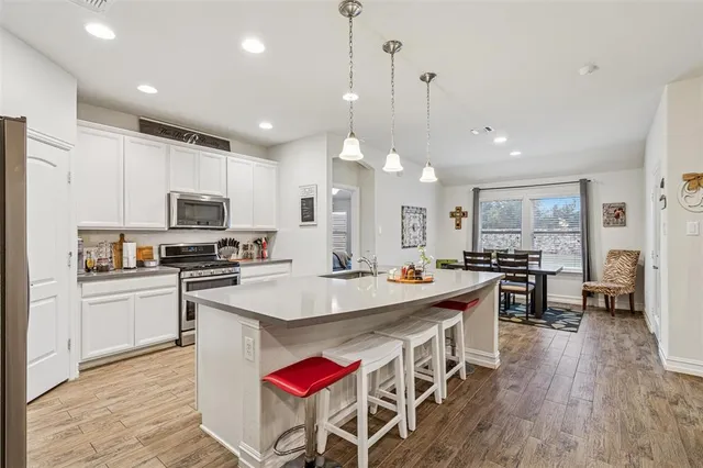 a kitchen with stainless steel appliances granite countertop a stove top oven a refrigerator a sink dishwasher and a dining table with wooden floor