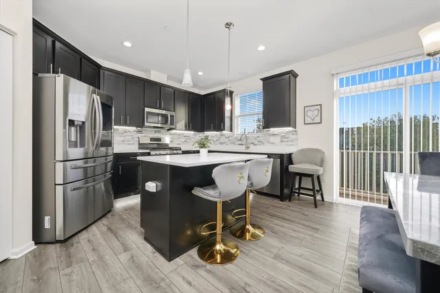 a kitchen with stainless steel appliances a dining table chairs refrigerator and cabinets