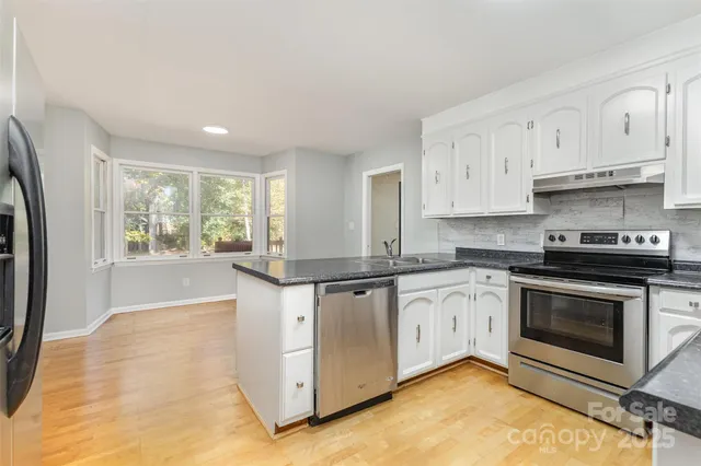 a kitchen with granite countertop white cabinets white appliances a sink and a window