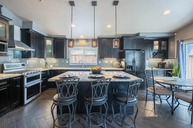 a kitchen with stainless steel appliances granite countertop a stove a refrigerator a kitchen island a table and chairs