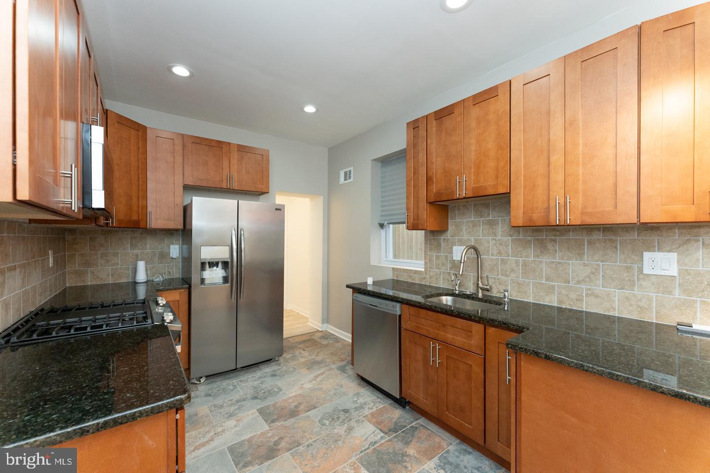 a kitchen with stainless steel appliances granite countertop wooden cabinets a stove a sink and a refrigerator