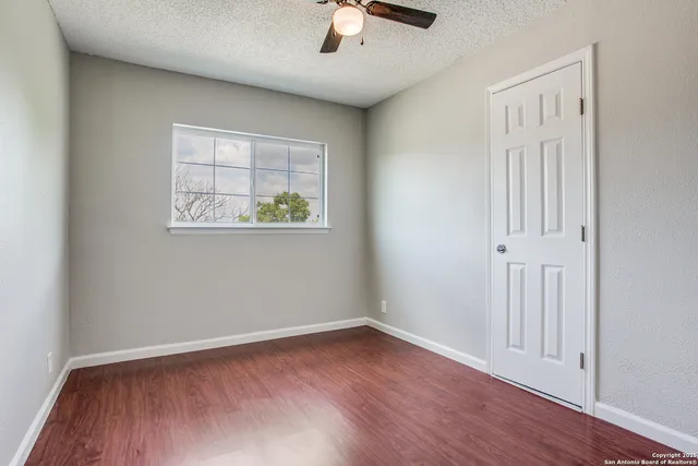 an empty room with wooden floor chandelier fan and windows