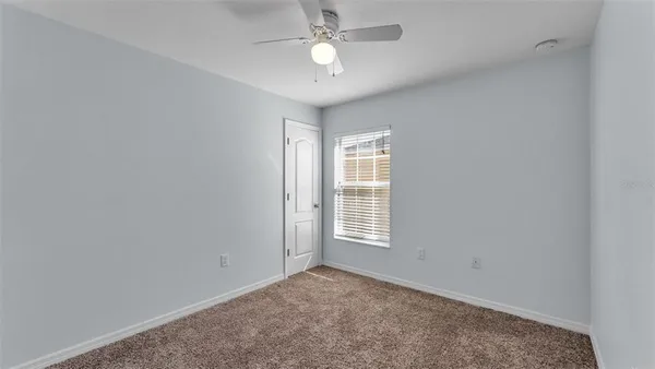 an empty room with chandelier fan and windows