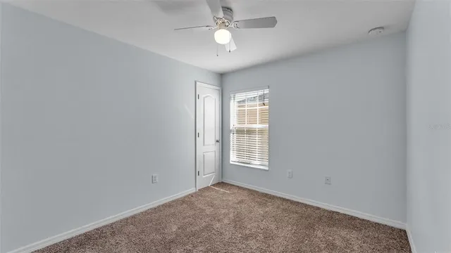 an empty room with chandelier fan and windows