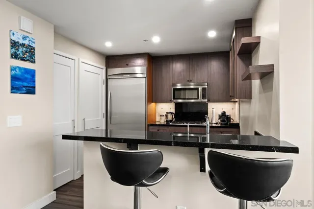 a living room with stainless steel appliances a dining table wooden floor and a view of kitchen