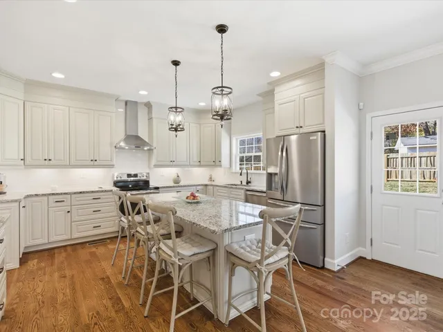 a kitchen with stainless steel appliances kitchen island granite countertop a refrigerator a stove a sink a dining table and chairs with wooden floor