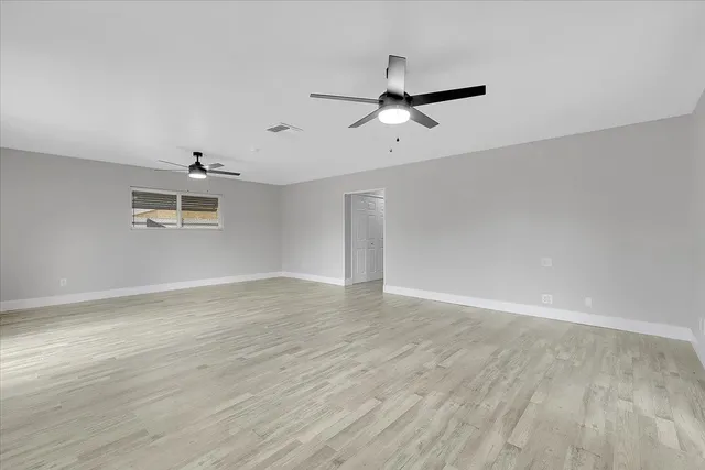 an empty room with wooden floor ceiling fan and windows