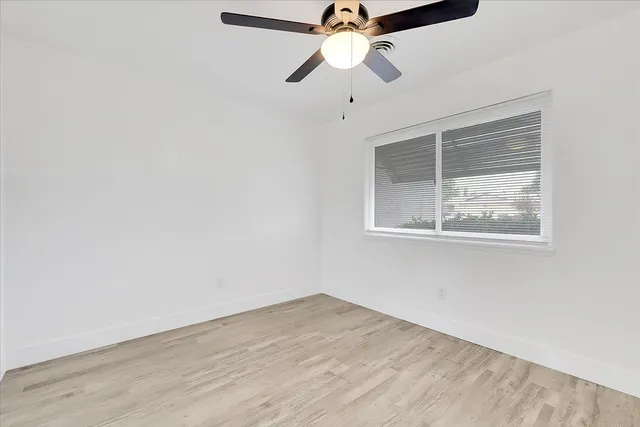 an empty room with wooden floor chandelier fan and windows
