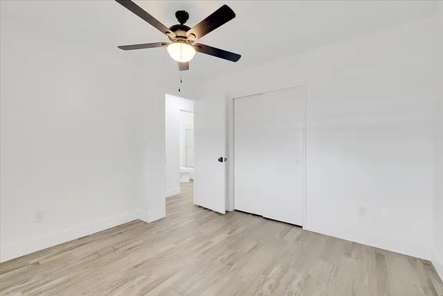 an empty room with wooden floor ceiling fan and window