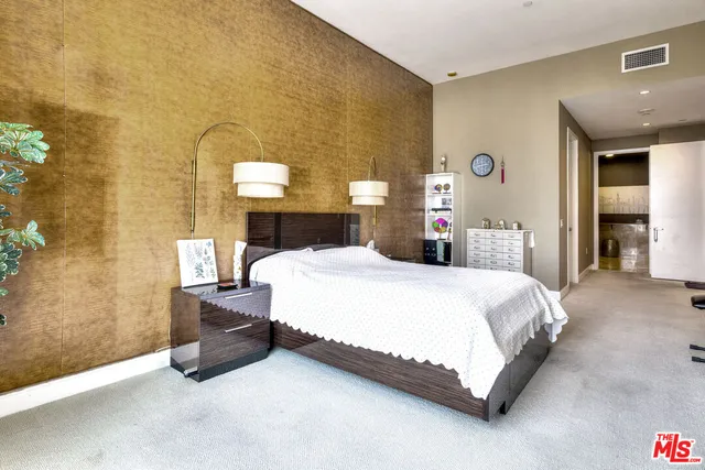 a bed sitting in a spacious bedroom next to a lamp