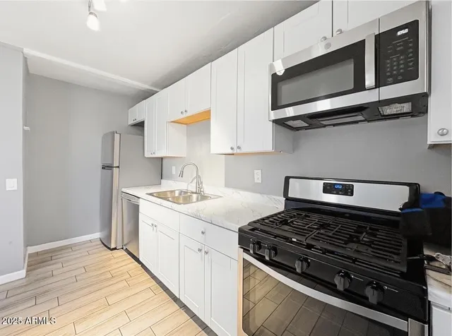 a kitchen with stainless steel appliances a sink dishwasher stove and microwave with wooden floor