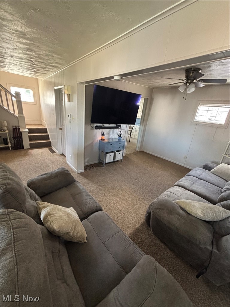 Carpeted living room with stairway, a wealth of natural light, a ceiling fan, and baseboards