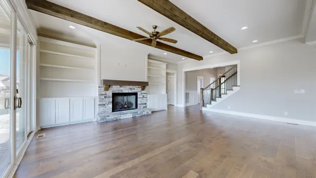 a view of a livingroom with wooden floor a fireplace a ceiling fan and windows